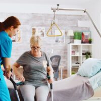 Old disabled lady walking with the help of crutches in nursing home