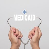 Hands holding a stethoscope and word "MEDICAID"  medical concept.