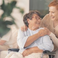 Smiling nurse supporting happy disabled elderly woman in the wheelchair