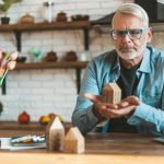 Preservation and restoration of real estate. A mature man holds a model of a house in his hands. Reflects before selling or buying a home. Mortgages and rental income.