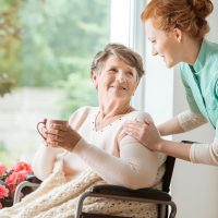 A professional caretaker in uniform helping a geriatric female p