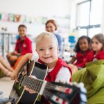 A down-syndrome boy with school kids and teacher sitting in class, playing guitar.