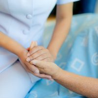 Nurse sitting on a hospital bed next to an older woman helping her