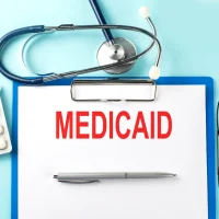 Paper with text MEDICAID on a blue background with stethoscope and pills
